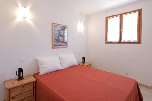 Chambre lumineuse à la RJD Conciergerie Côte d'Azur avec édredon rouge, tables de nuit en bois et grande fenêtre avec vue
