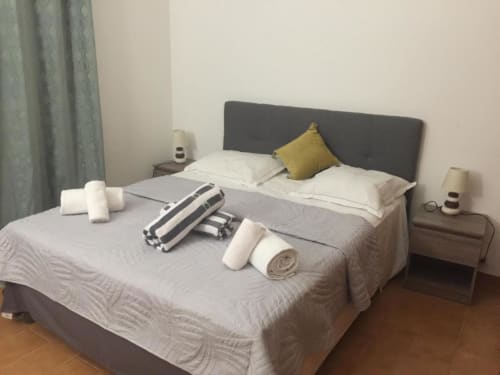 Chambre moderne à la RJD Conciergerie Côte d'Azur avec tête de lit grise, literie blanche, coussin jaune et équipements