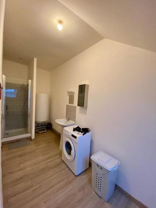 Salle de bains moderne dans l'appartement Business Apparts Caudry avec lave-linge, lavabo, douche et équipements blancs sur bois