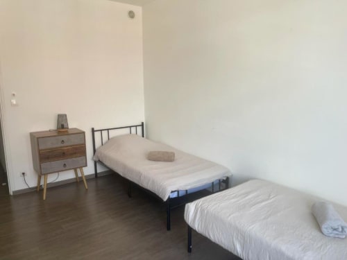 Deux lits simples avec table de nuit en bois dans l'appartement Business Apparts Caudry, parquet, murs blancs