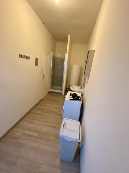 Couloir étroit de l'appartement Business Apparts Caudry avec bacs de rangement bleus, lavabo blanc et accès à la salle de bain