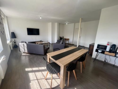 Appartement 2 chambres moderne à Business Apparts Caudry avec table à manger, coin salon, cuisine et TV écran plat