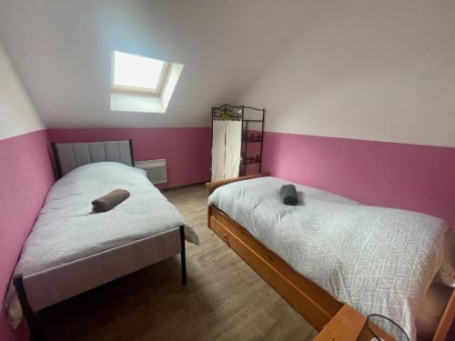 Deux lits simples avec draps blancs dans une chambre mansardée lumineuse aux murs rose et blanc à Business Apparts Caudry, Caudry