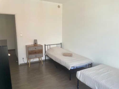 Lits jumeaux aux draps blancs dans la chambre de Business Apparts Caudry, commode en bois, parquet, décoration minimaliste