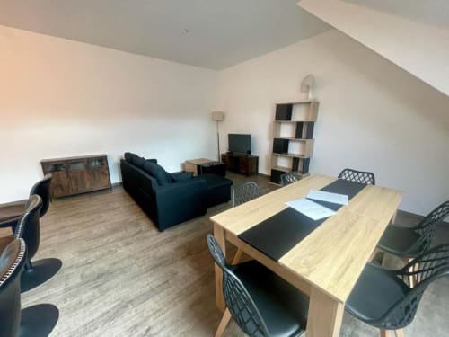 Appartement 2 chambres à Business Apparts Caudry avec table à manger, canapé, télévision et étagères dans le séjour ouvert