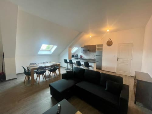 Appartement moderne 2 chambres à Business Apparts Caudry, séjour ouvert avec canapé noir, table à manger, cuisine et puits de lumière
