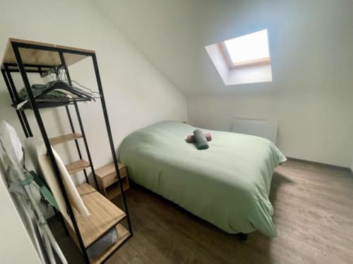 Chambre lumineuse sous les toits aux Business Apparts Caudry avec puits de lumière, literie verte et portant en métal noir sur parquet.