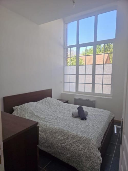 Chambre lumineuse à Business Apparts Caudry avec lit double, grandes fenêtres sur la ville et mobilier moderne