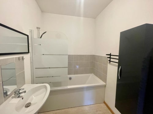 Salle de bain moderne dans l'appartement Business Apparts Caudry avec baignoire blanche, paroi de douche vitrée, lavabo rond et carrelage beige