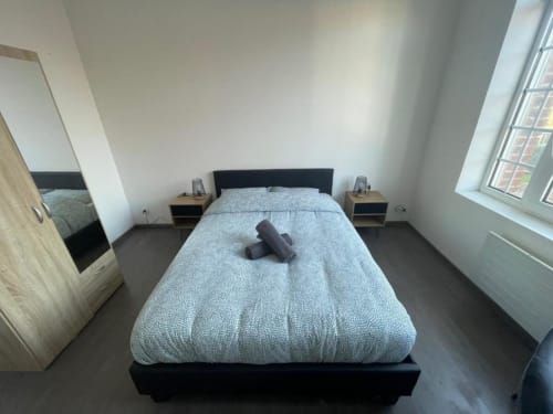 Chambre moderne à Business Apparts Caudry avec lit queen-size, tête de lit noire, tables de nuit en bois et vue sur la ville