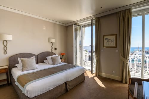 Camera di lusso dell'Hotel Splendid Cannes con balcone vista mare, letto king e costa mediterranea visibile attraverso le vetrate