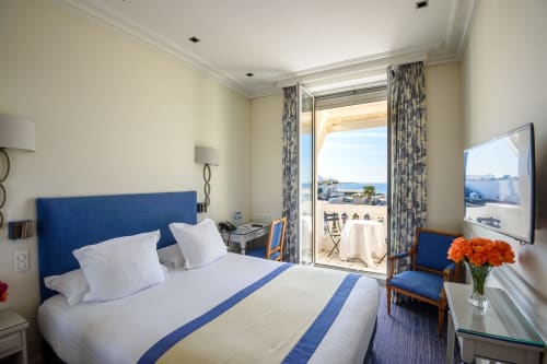Elegante camera d'hotel a Cannes con vista sul mare, testata blu, biancheria bianca, balcone sulla Mediterranea, TV schermo piatto