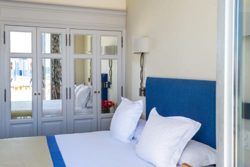 Camera d'hotel luminosa con testata imbottita blu, biancheria bianca, porte dell'armadio specchiate e vista sul mare all'Hotel Splendid