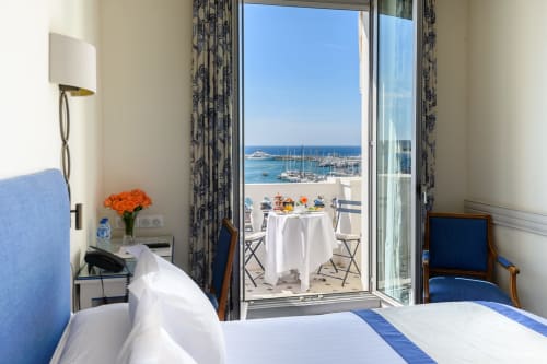 Camera da letto luminosa all'Hotel Splendid Cannes con vista sul mare della marina e barche a vela attraverso porte in vetro che si aprono sulla terrazza