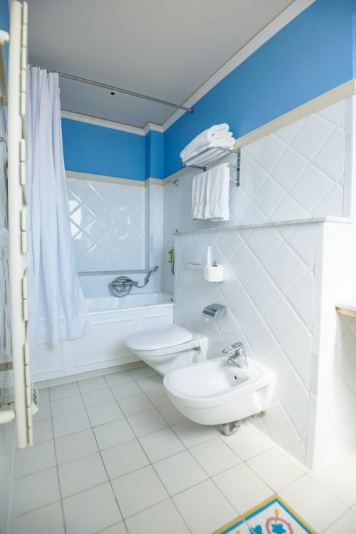 Bagno moderno con pareti superiori blu, piastrelle in stile metro bianche, WC, bidet e vasca da bagno con tenda doccia all'Hotel Splendid