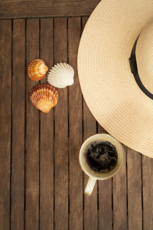 Chapeau de paille, coquillages et tasse de café sur la terrasse en bois de La Maison du Potier, Valras-Plage