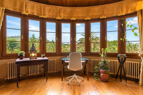 Elegante suite de oficina con curvas, muebles de madera, silla blanca, vistas panorámicas al jardín y cortinas doradas en Basque