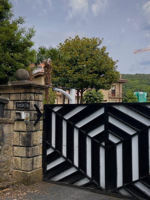 Entrada elegante de la Casa Señorial Sasueta en blanco y negro con pilar de piedra y vegetación exuberante