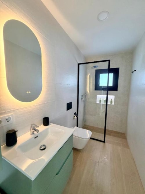 Baño moderno en Villa Rua C de Barrosa Home con espejo iluminado, ducha abierta y piso de madera