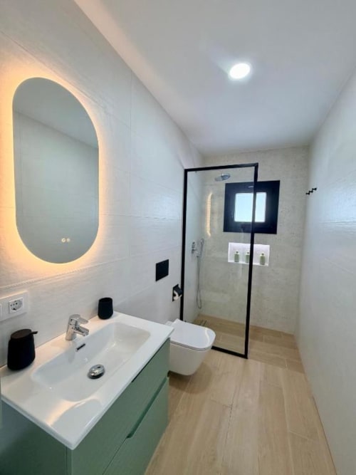 Cuarto de baño moderno en Villa Rua C de Barrosa Home, Chiclana de la Frontera, con espejo ovalado iluminado, lavamanos blanco y