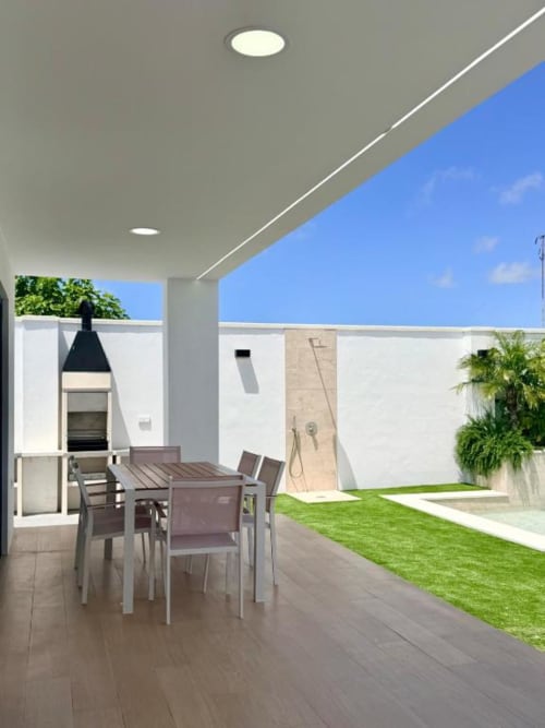 Terraza de villa moderna en Barrosa Home con mesa de comedor, vistas al jardín y piscina privada bajo cielo despejado
