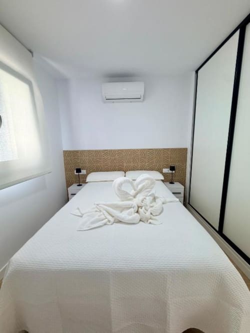 Dormitorio moderno en la villa Barrosa Home de Chiclana de la Frontera con ropa de cama blanca, cabecero estampado y aire acondicionado