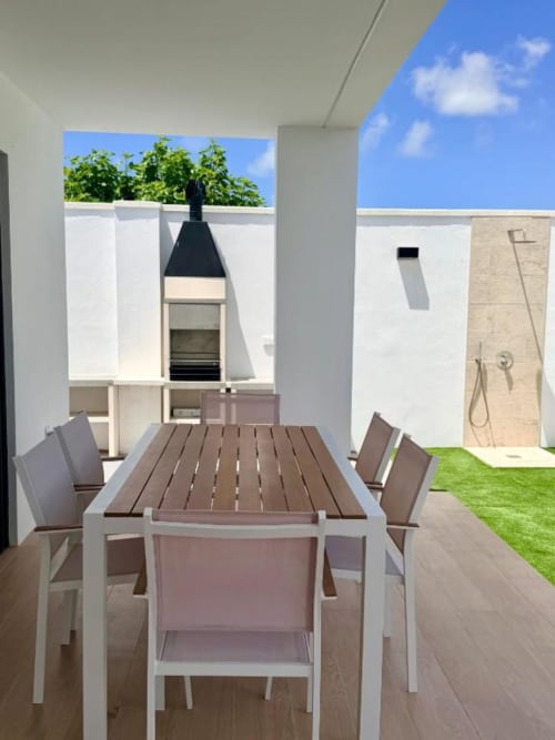 Terraza de villa moderna con mesa de comedor, sillas y parrilla cónica negra en Barrosa Home Chiclana, con vistas al jardín privado
