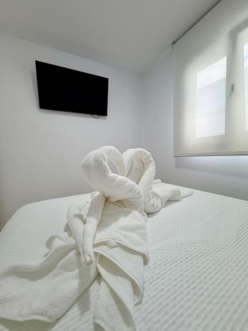 Escultura de cisne de toalla blanca sobre cama en dormitorio de villa moderna Barrosa Home con TV de pantalla plana y luz natural