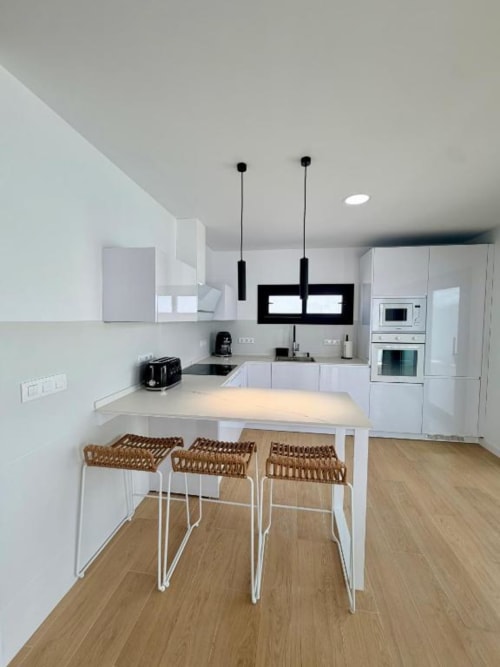Moderna cocina blanca en Villa Rua C de Barrosa Home, Chiclana de la Frontera, con barra isla, lámparas colgantes y