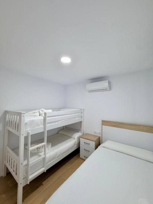 Dormitorio moderno en villa Barrosa Home, Chiclana, con literas blancas, cama individual, aire acondicionado y suelo de madera