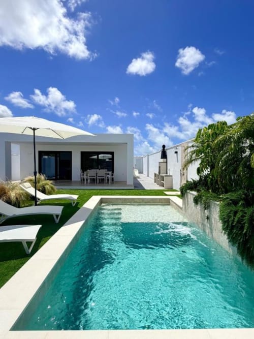 Villa moderna con piscina privada turquesa, tumbonas blancas y jardín verde en Barrosa Home, Chiclana