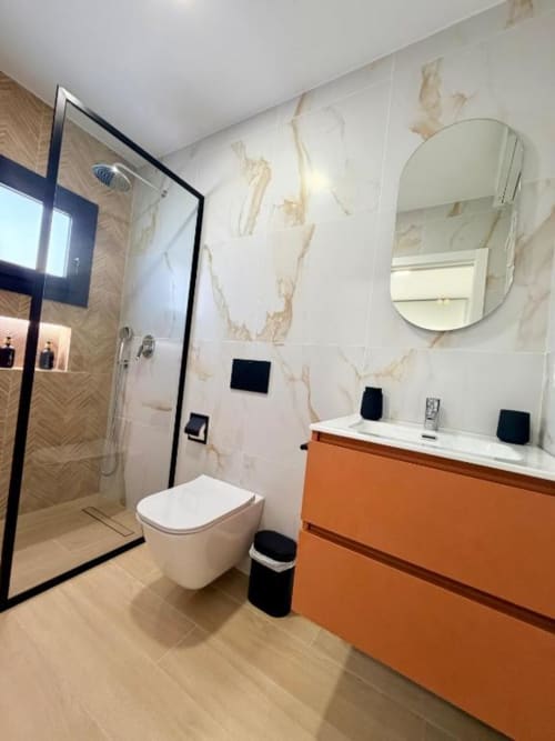 Baño moderno en Villa Rua C de Barrosa Home con vanidor naranja, inodoro blanco, azulejos de mármol y ducha abierta