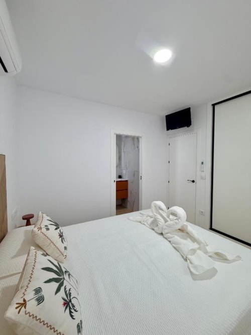 Moderno dormitorio en Villa Rua C de Barrosa Home, Chiclana de la Frontera, con cama blanca y toallas de bienvenida
