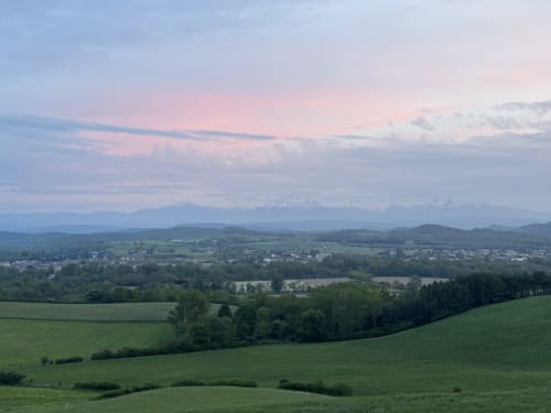 Vue panoramique de la vallée depuis le Domaine de Bize à Mirepoix, Ariège avec champs verts, village en contrebas et montagnes enneigées