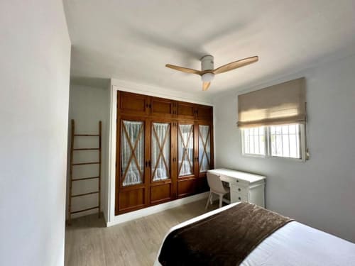 Dormitorio luminoso en Villa Faro, Hozanejos, con armario de madera, escritorio, ventilador de techo y vistas al jardín