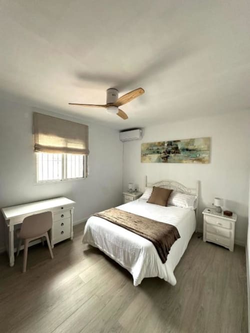 Dormitorio moderno en Villa Faro, Barrosa Home, con cama, escritorio, ventilador de techo, aire acondicionado y vistas al jardín