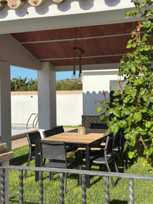 Área de comedor en terraza cubierta de Villa Faro con mesa de madera, sillas negras, vistas al jardín y piscina privada al fondo