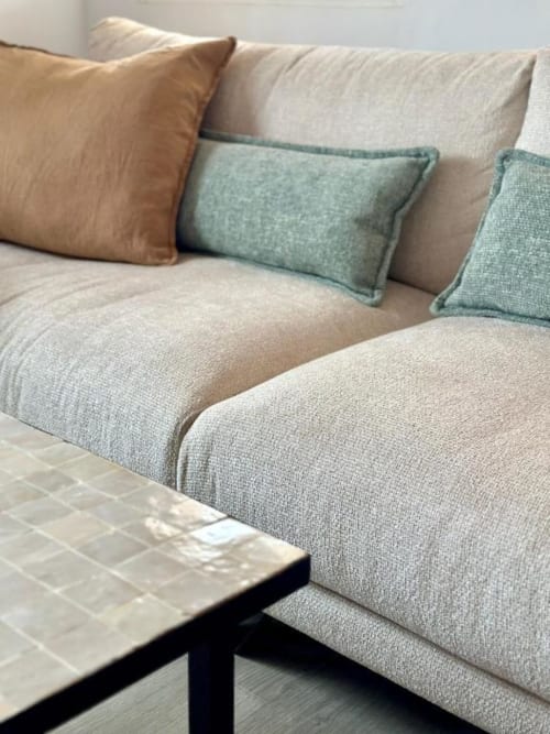 Sofá tapizado en beige con cojines decorativos en tonos tostado y verde salvia en Villa Faro, Barrosa Home, Hozanejos