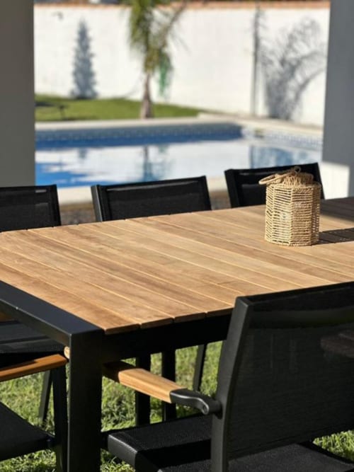 Mesa de comedor exterior con tapa de madera y sillas negras junto a piscina privada en Villa Faro, Barrosa Home