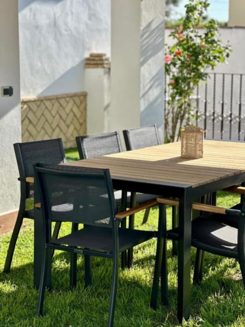 Terraza de comedor al aire libre en Villa Faro, Barrosa Home, con sillas negras y mesa de madera con vistas al jardín en Hozanejos
