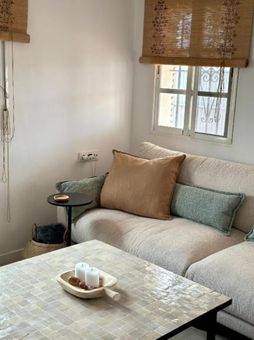 Elegante sala de estar en villa Barrosa Home con sofá beige, cojín marrón, almohadas en tonos turquesas, mesita negra y vista al jardín
