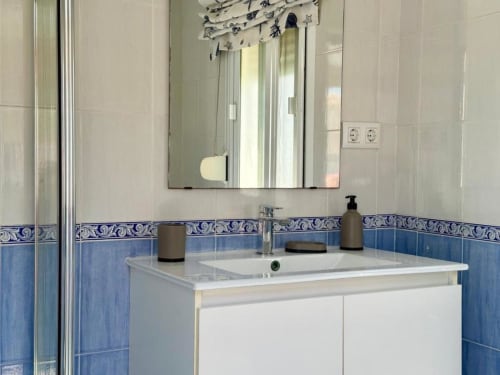 Lavamanos moderno y espejo en Villa Faro de Barrosa Home, Hozanejos, con detalles en azulejos azules y ventana con vista al jardín