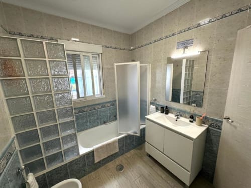 Baño moderno en Barrosa Home Villa Faro con ducha de cristal, lavabo blanco y paredes alicatadas
