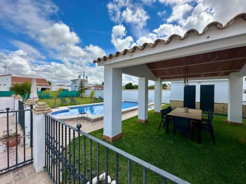 Patio trasero de Villa Faro con piscina privada, terraza cubierta, comedor y jardín cuidado en Barrosa Home, Hozanejos, España