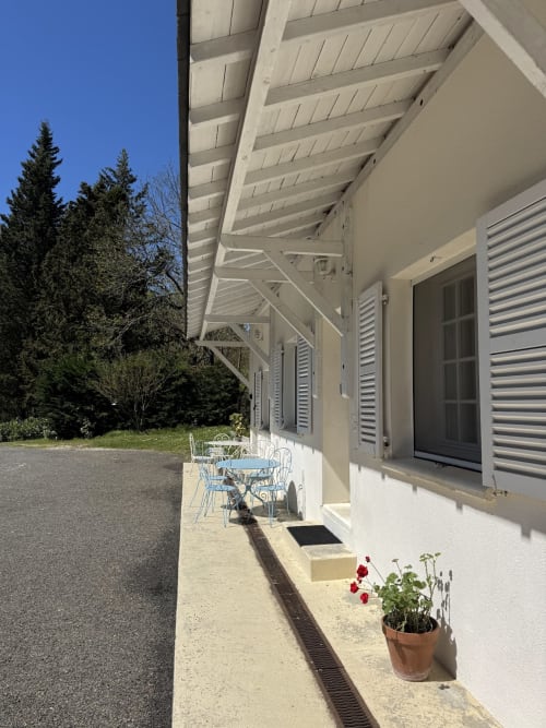 Terrasse moderne du Domaine de Bize avec pergola blanche, salon de jardin, fleurs rouges et vue forêt à Mirepoix