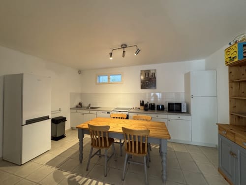 Cuisine moderne et lumineuse avec table à manger en bois, quatre chaises, meubles blancs et appareils inox au Domaine de