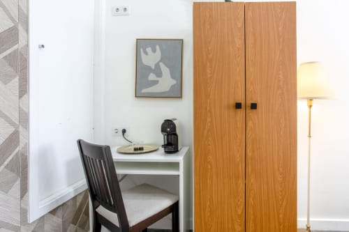 Lisbon Poets Inn hostel suite desk area with wooden wardrobe, black chair, artwork, and floor lamp