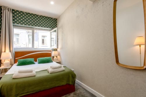 Modern bedroom at Lisbon Poets Inn with wood headboard, green accents, city view window, and brass mirror
