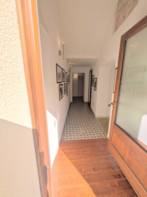 Corridoio dell'Albergo Al Cinghiale con pavimento in legno, pareti bianche, quadri incorniciati e mattonelle decorate