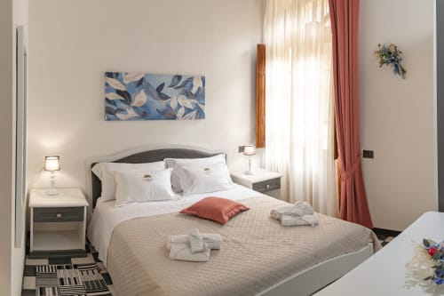 Spaziosa camera doppia dell'Albergo Al Cinghiale con biancheria beige, opere d'arte blu, tende in terracotta e arredi moderni